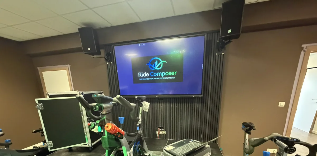 Une salle d'indoor cycling, les vélos face à un écran mural piloté par RideComposer depuis un portable